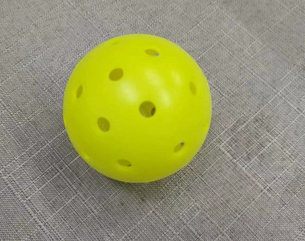 Creative Vault Marketplace yellow pickleball with 40 holes for indoor and outdoor play on a textured fabric surface